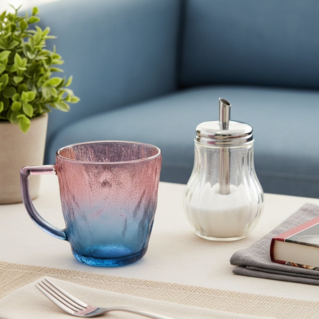 Colorful mug with a salt shaker and book on a table with a plant in the background