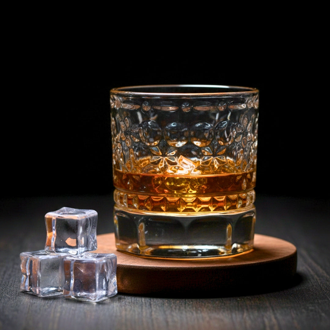 Glass of whiskey with ice cubes on a dark surface